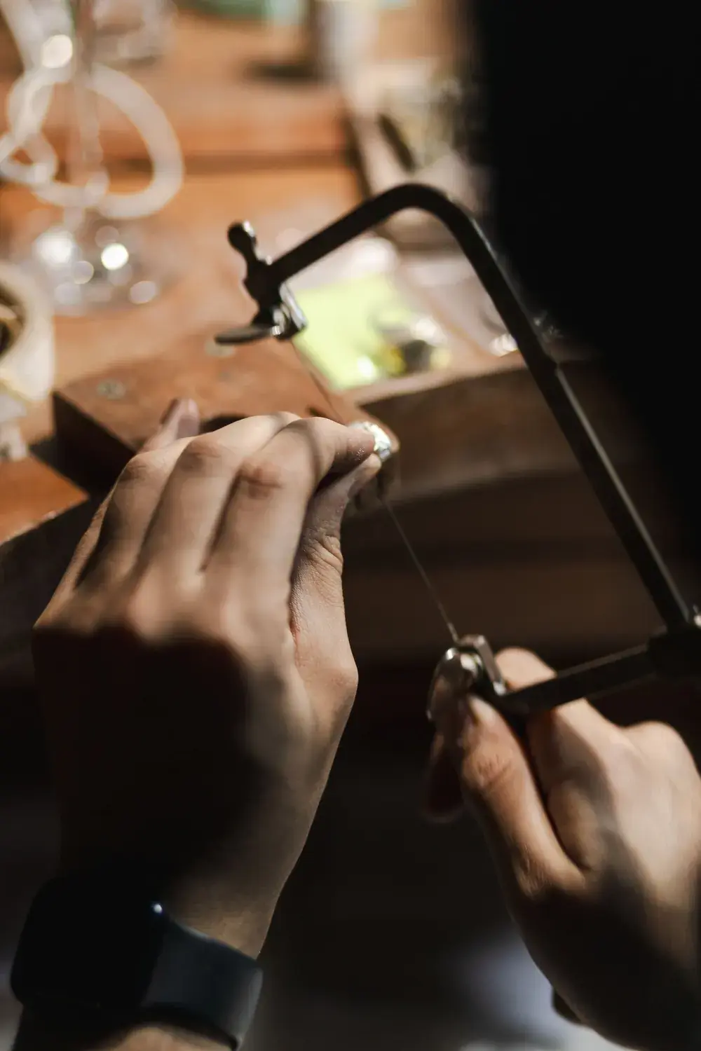 A jeweller's hands holding a saw frame against a piece at the bench.