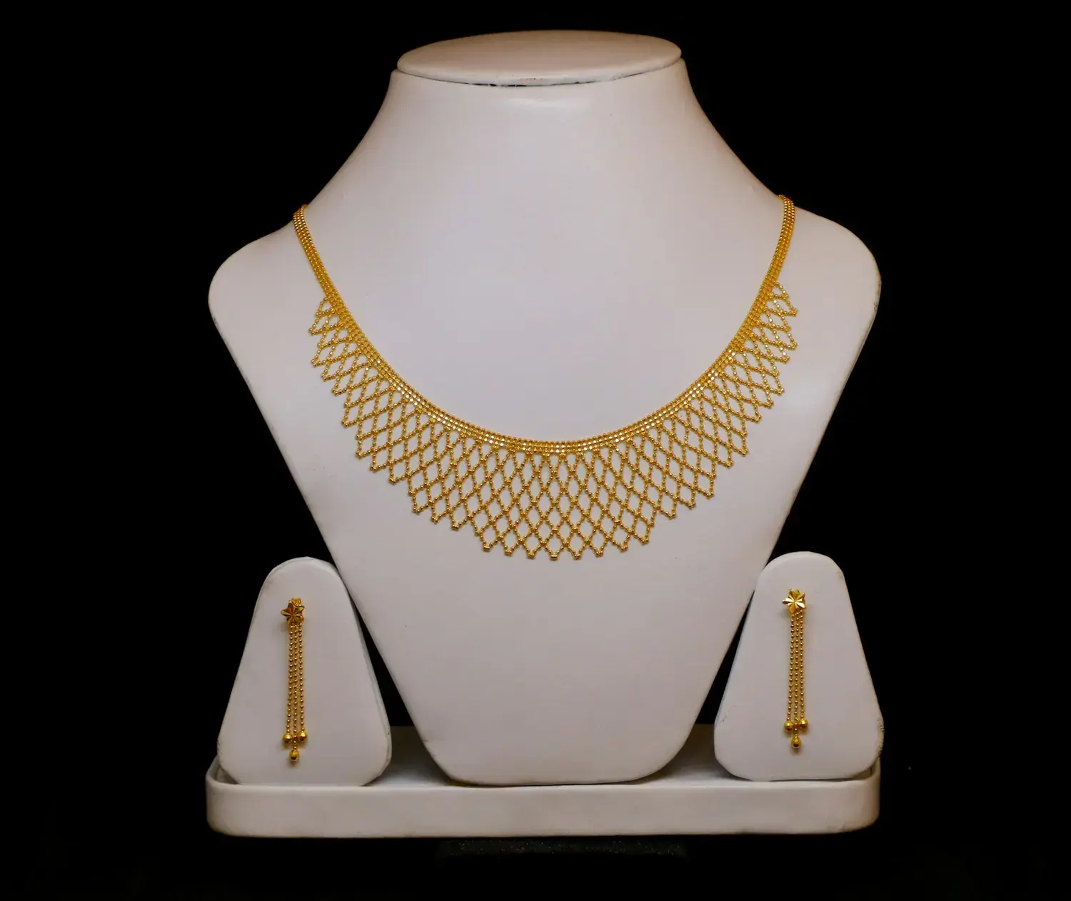 A gold collar necklace displayed on a pale bust against a dark ground.
