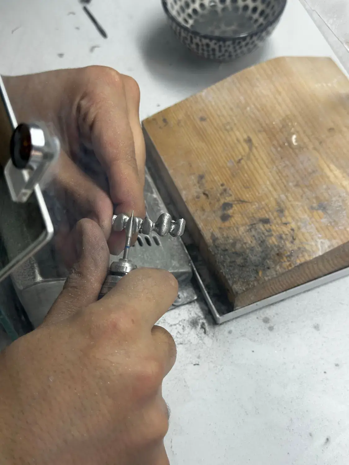 A jeweller's hands working a silver ring at the bench.