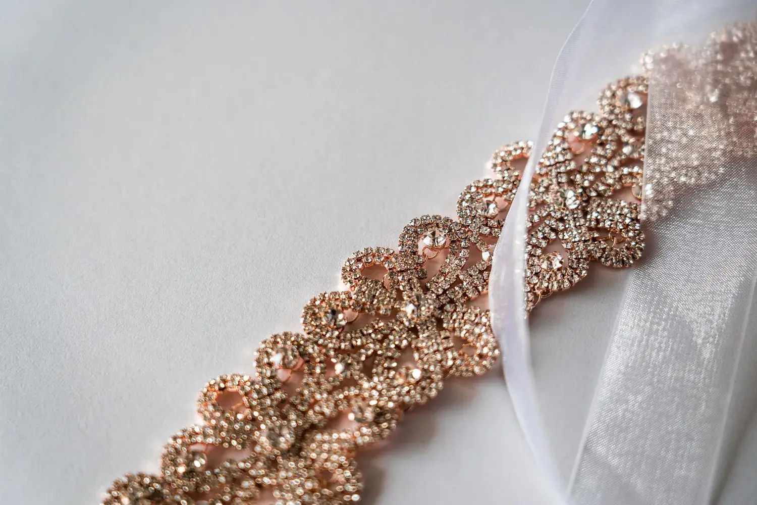 A rose gold necklace set with stones, laid on sheer white fabric.