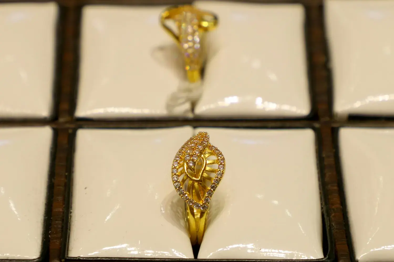 Two ornate gold rings set with stones, resting on a pale cushioned tray.
